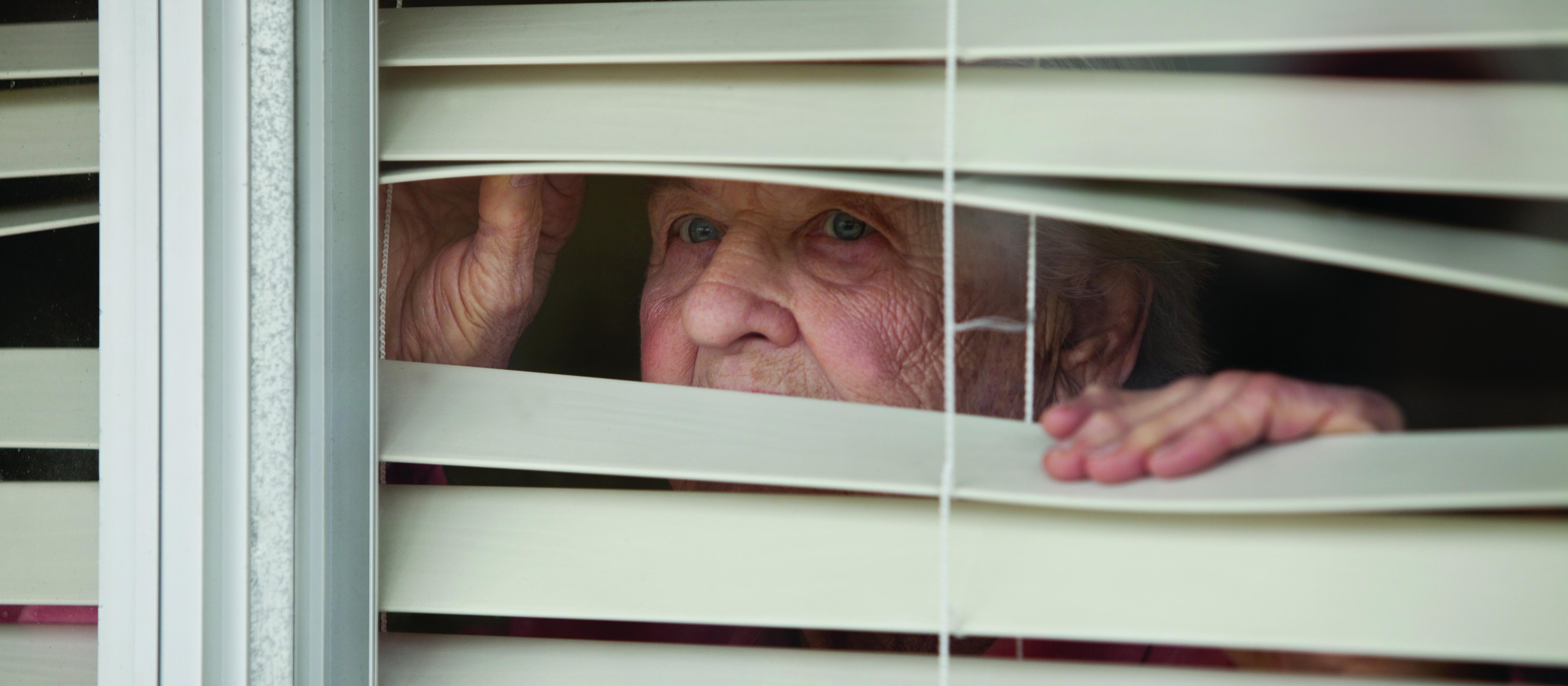 Elderly woman looks through blinds