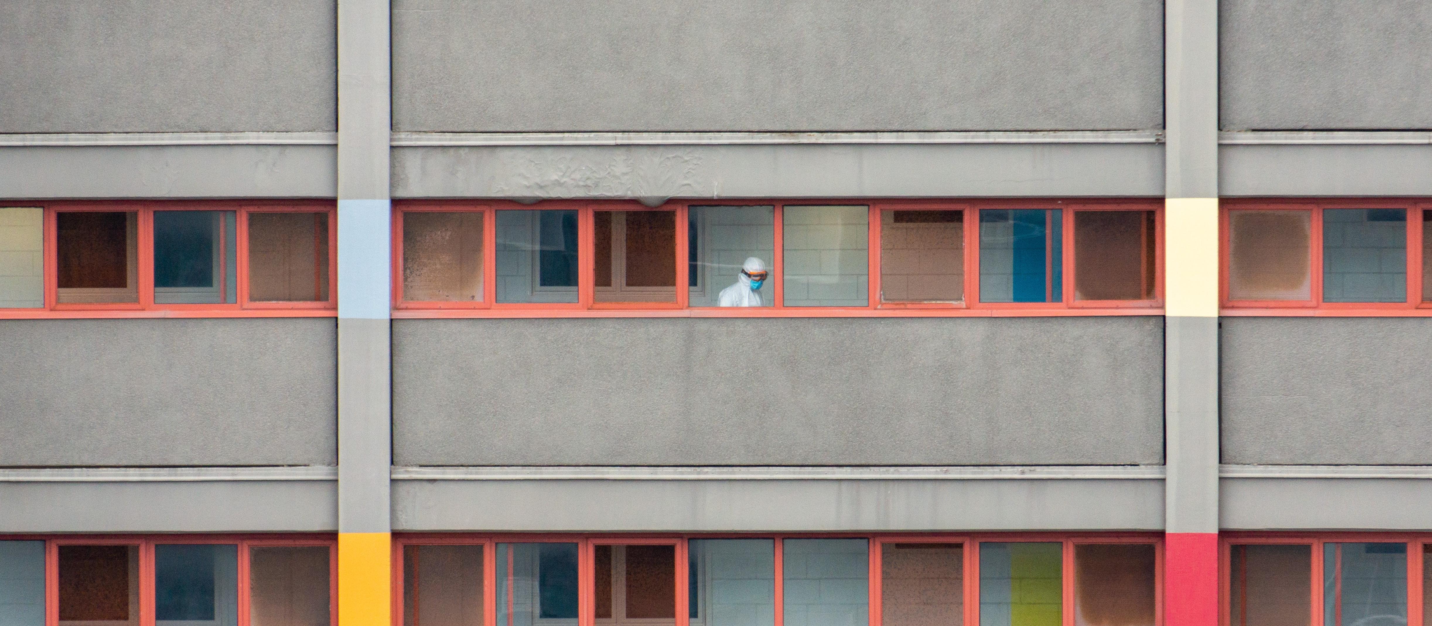  A worker in full PPE walks down the hallway of a locked down residential housing tower in North Melbourne, Victoria, Australia [Image: Chris McLay on Unsplash]