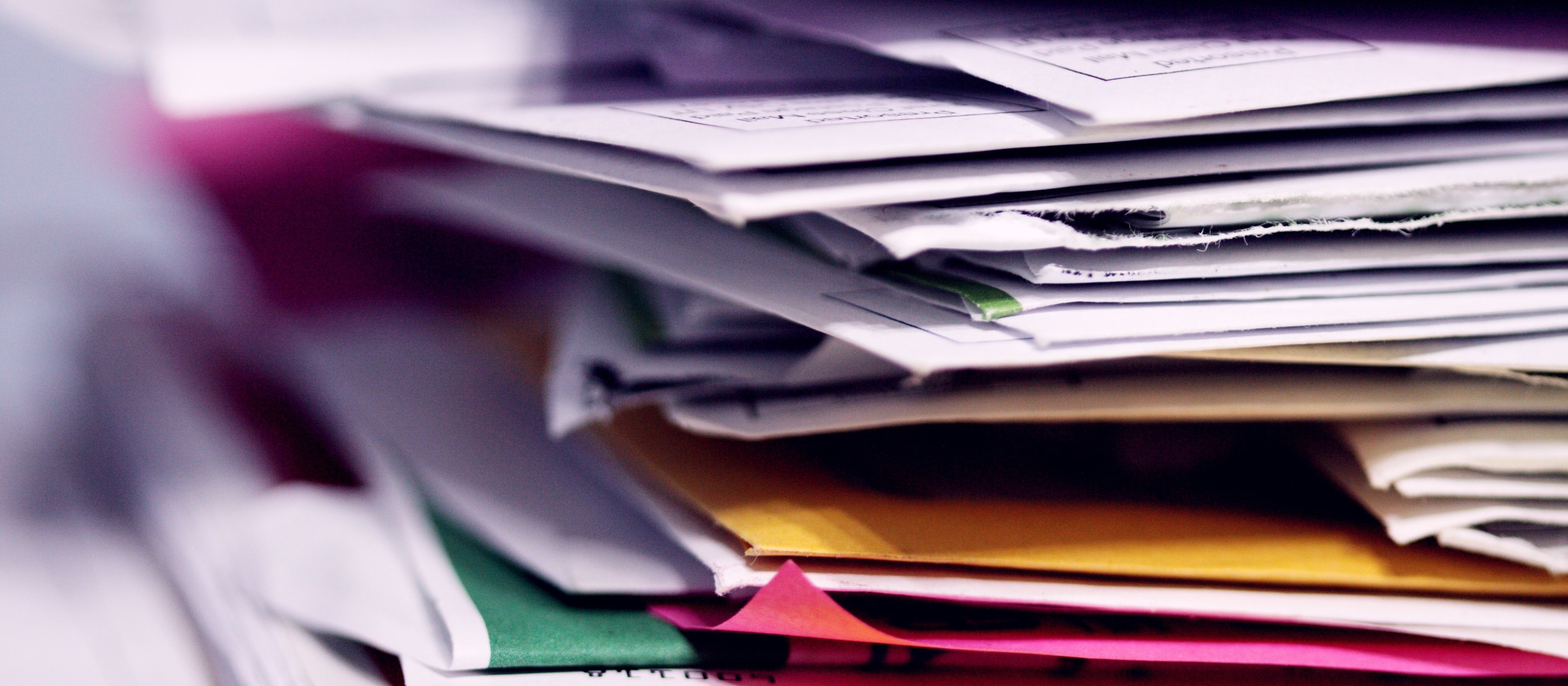 Image shoes a stack of documents and reports, some in colourful folders