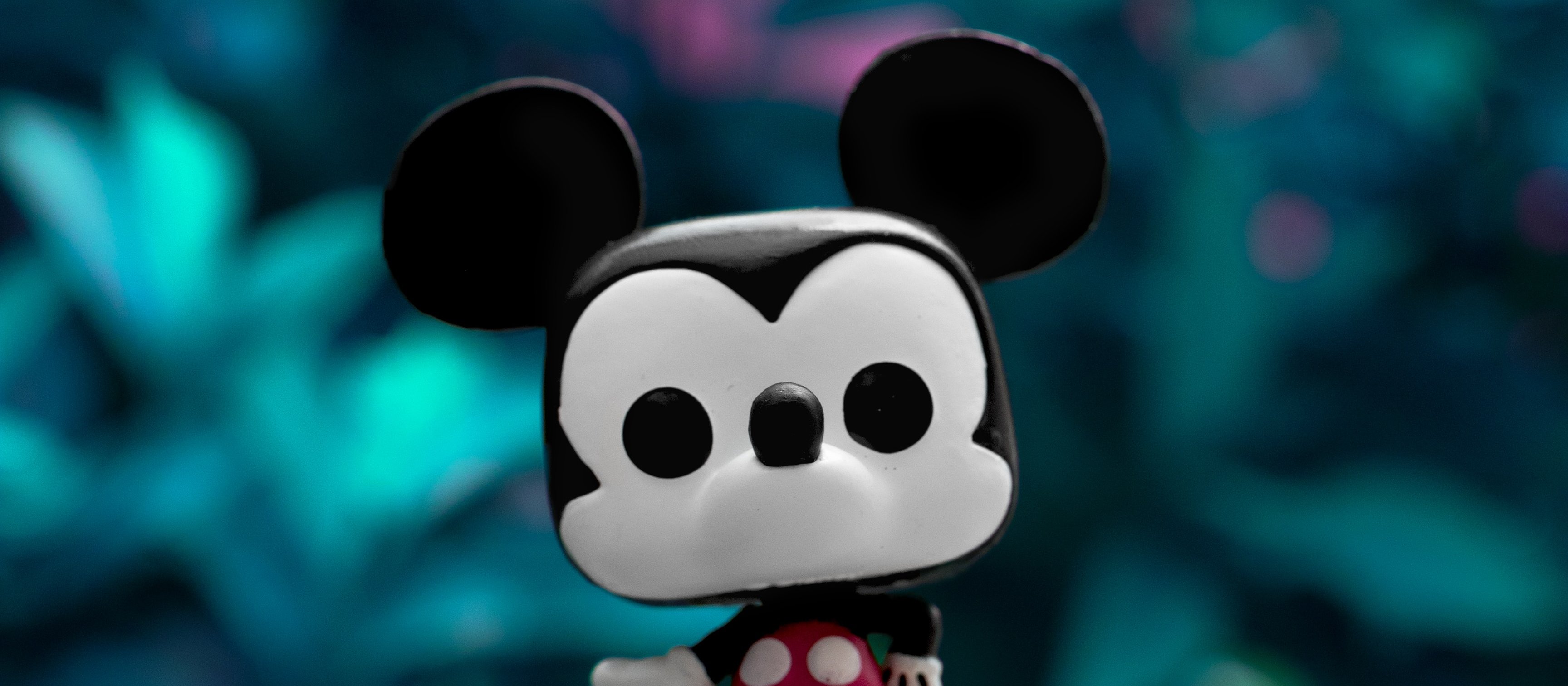 A small Mickey Mouse toy set on a rock, with foliage in background