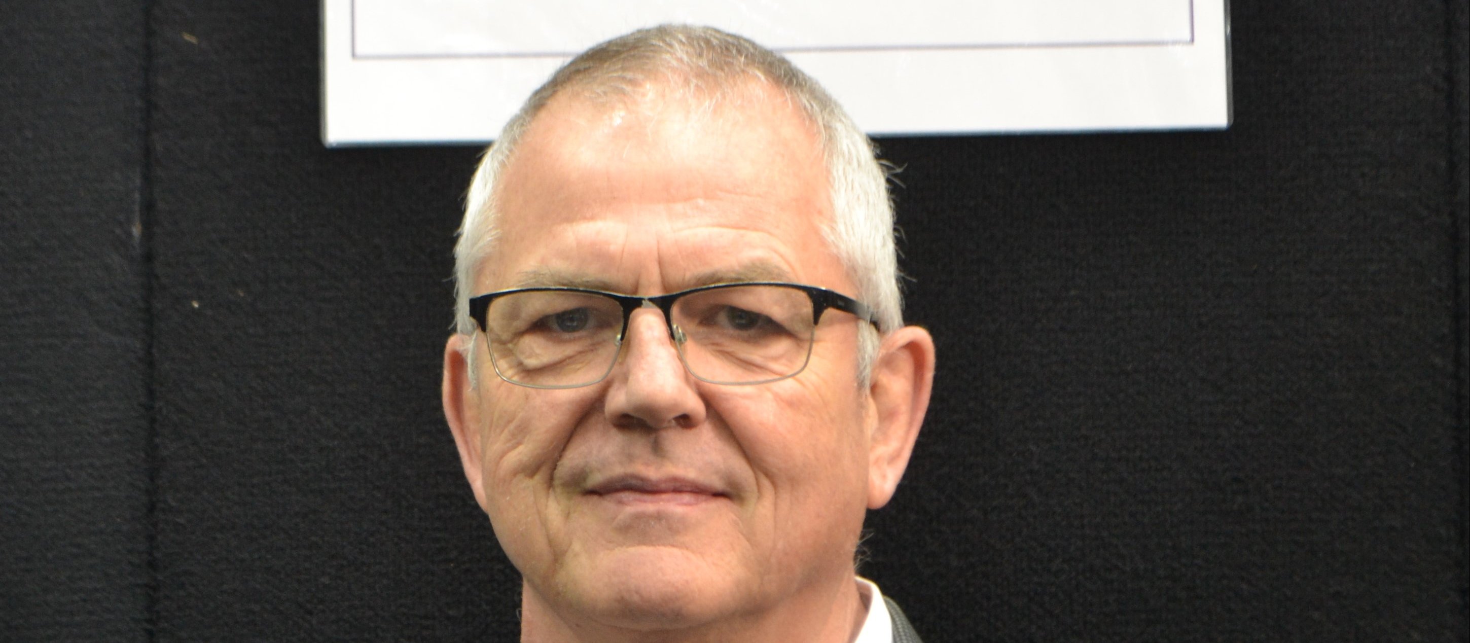 Man with glasses looking at camera, sign above head reads Compound Labs