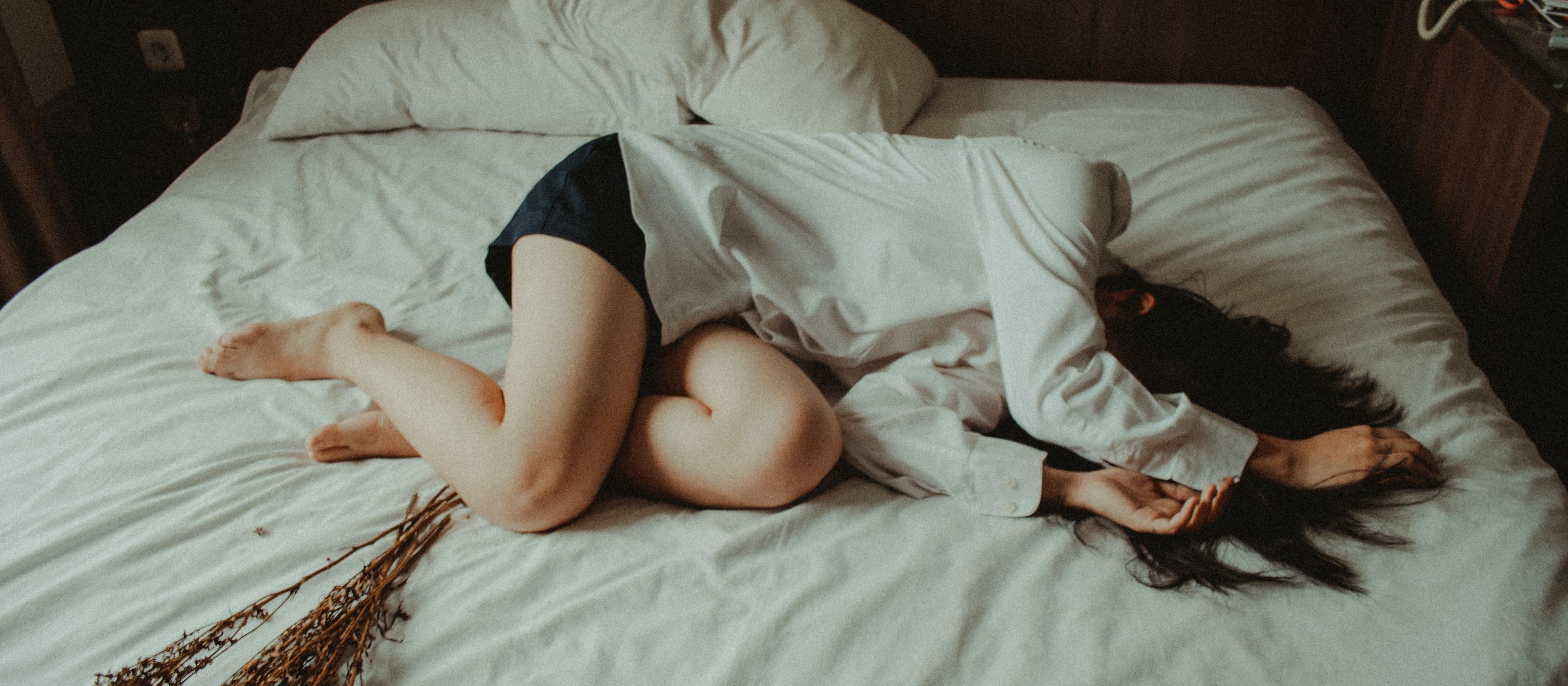 Woman lies on a bed, with her hands over her head