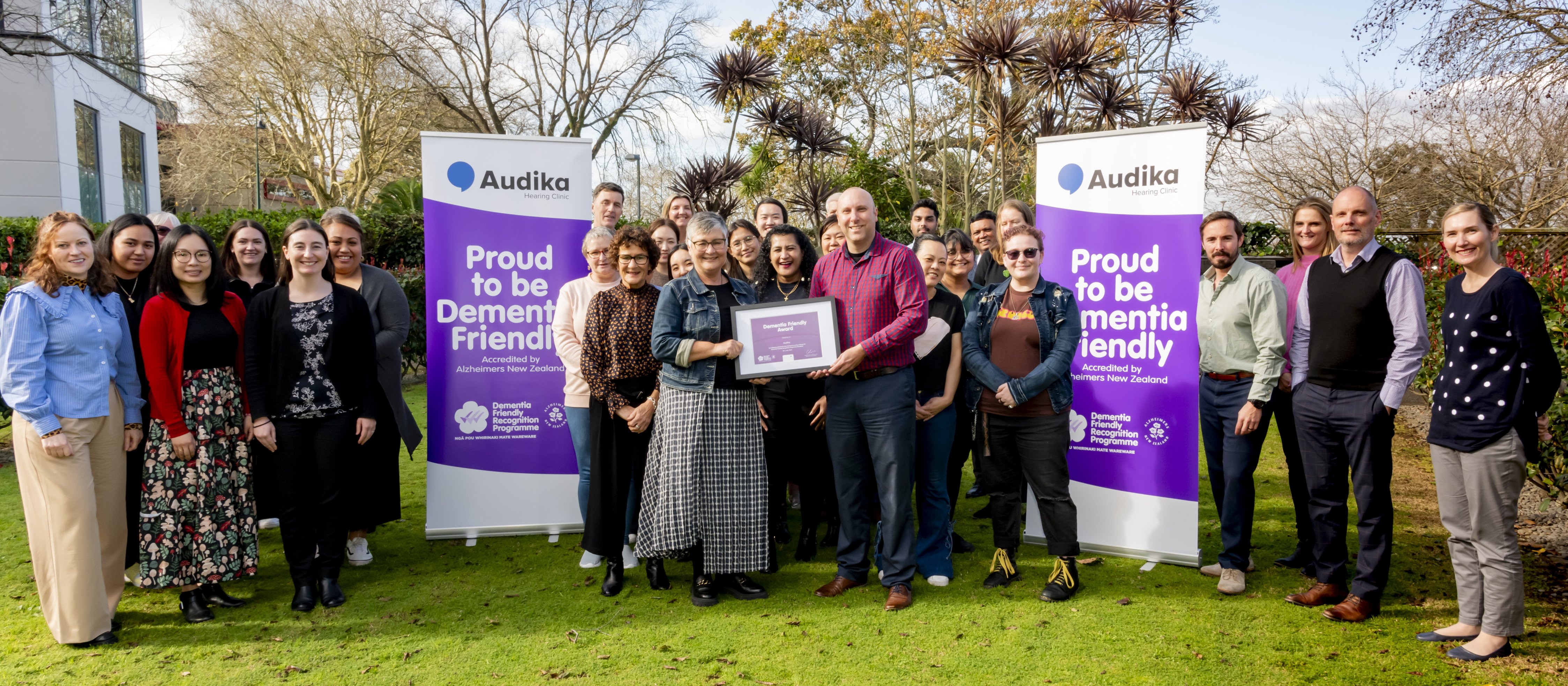 A group of people standing on lush grass, two in the middle holding up a framed certificate