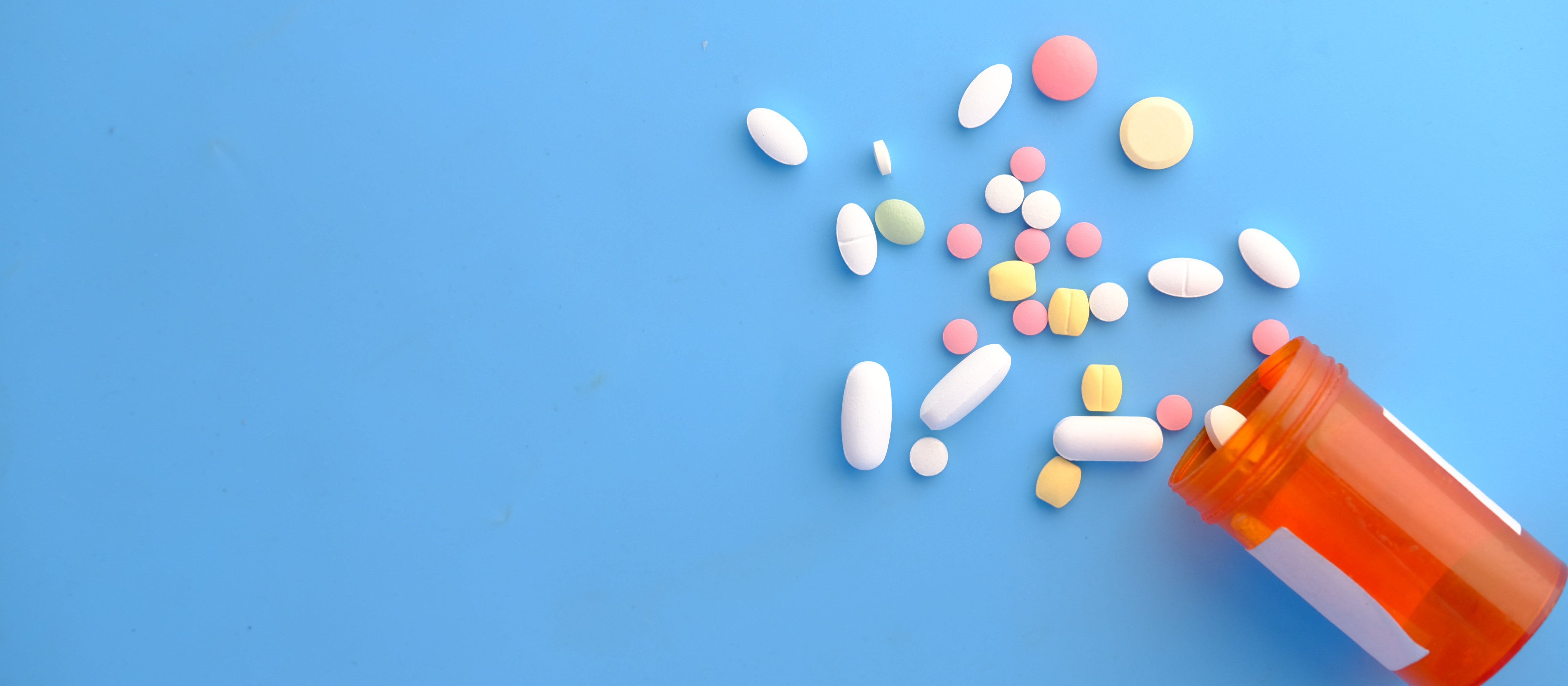 Different coloured pills spilling out of a medication jar on a blue background