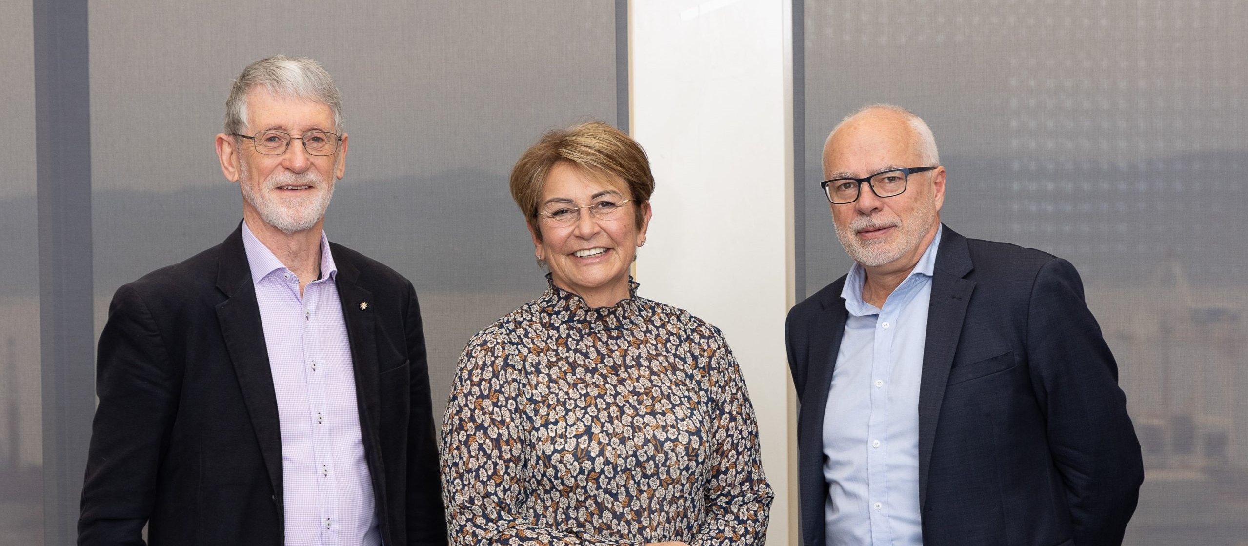 Image shows a woman in printed dress standing between two men in suits