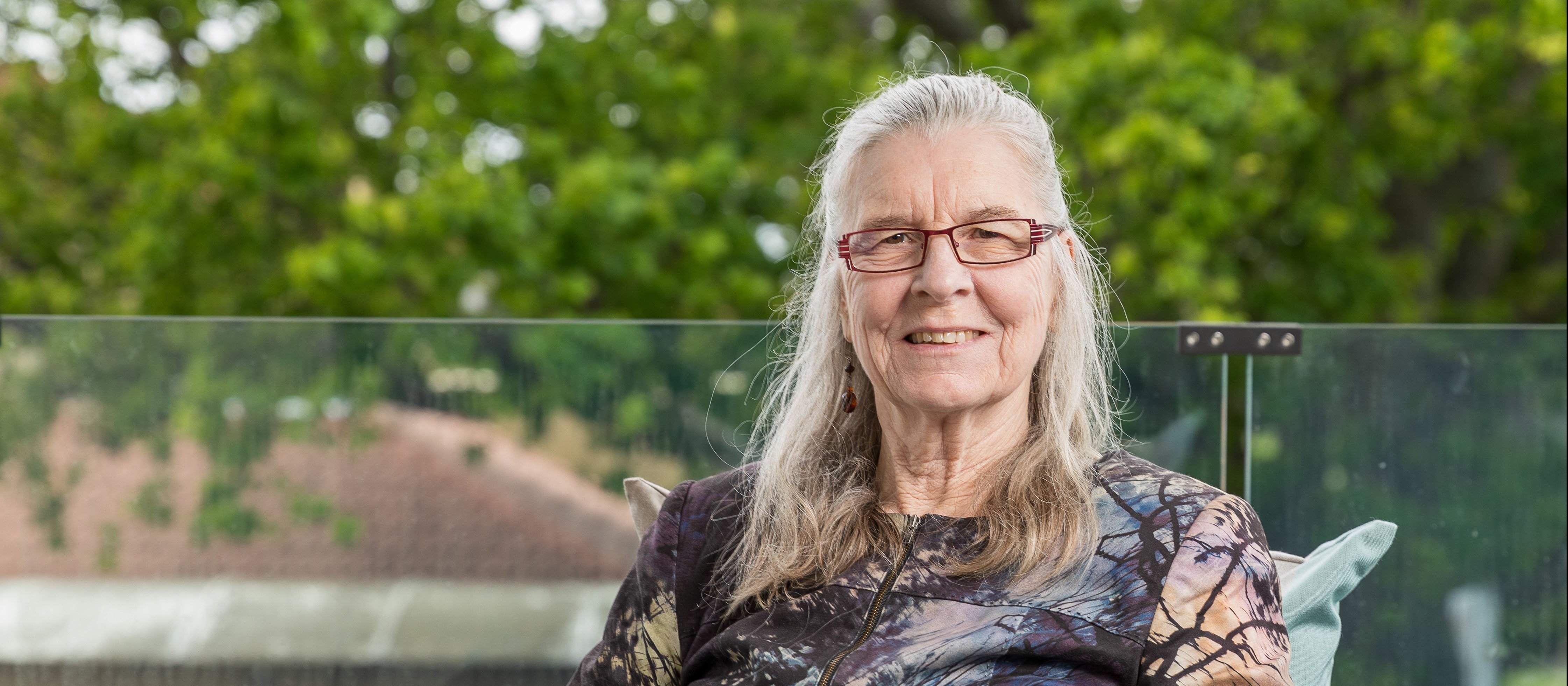 Amanda Oakley sits in a black rattan chair with trees in background