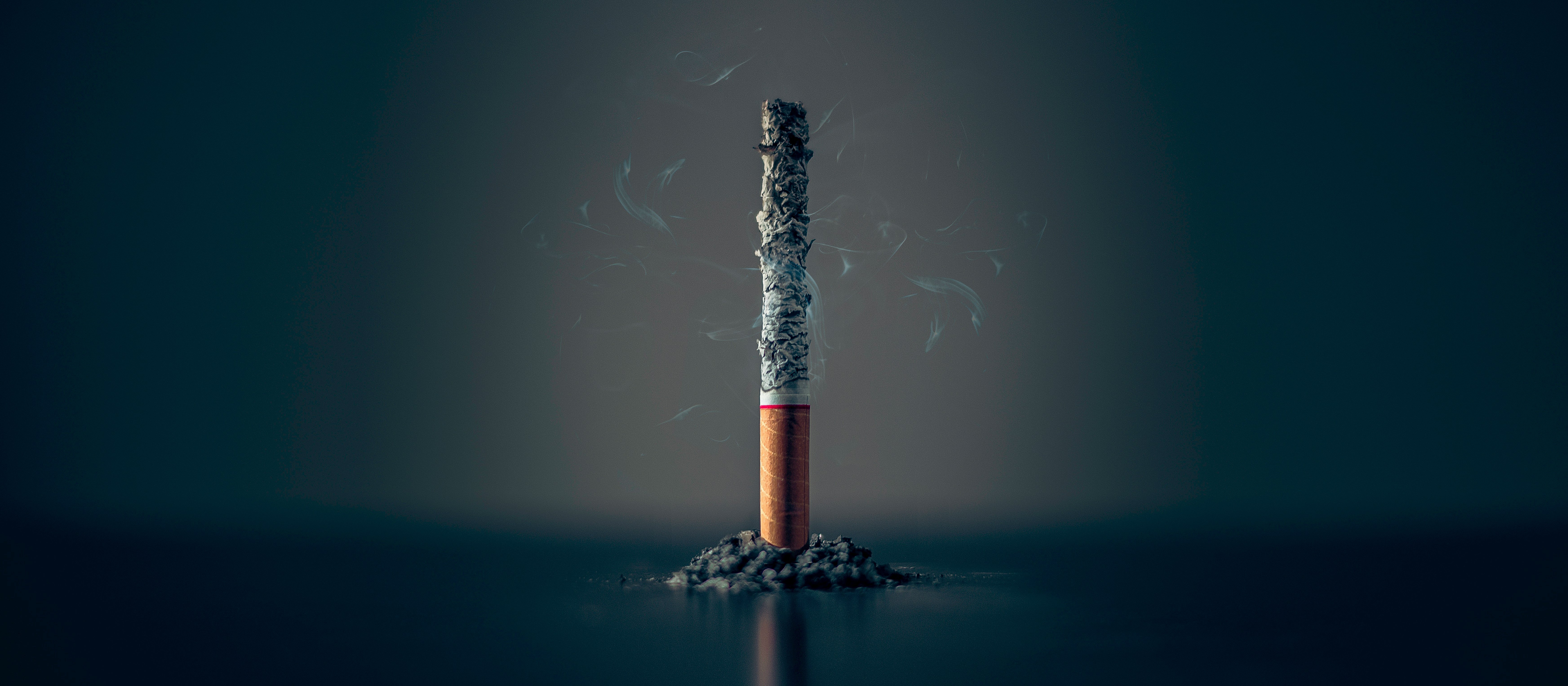 A single cigarette stands on end, with a black background 