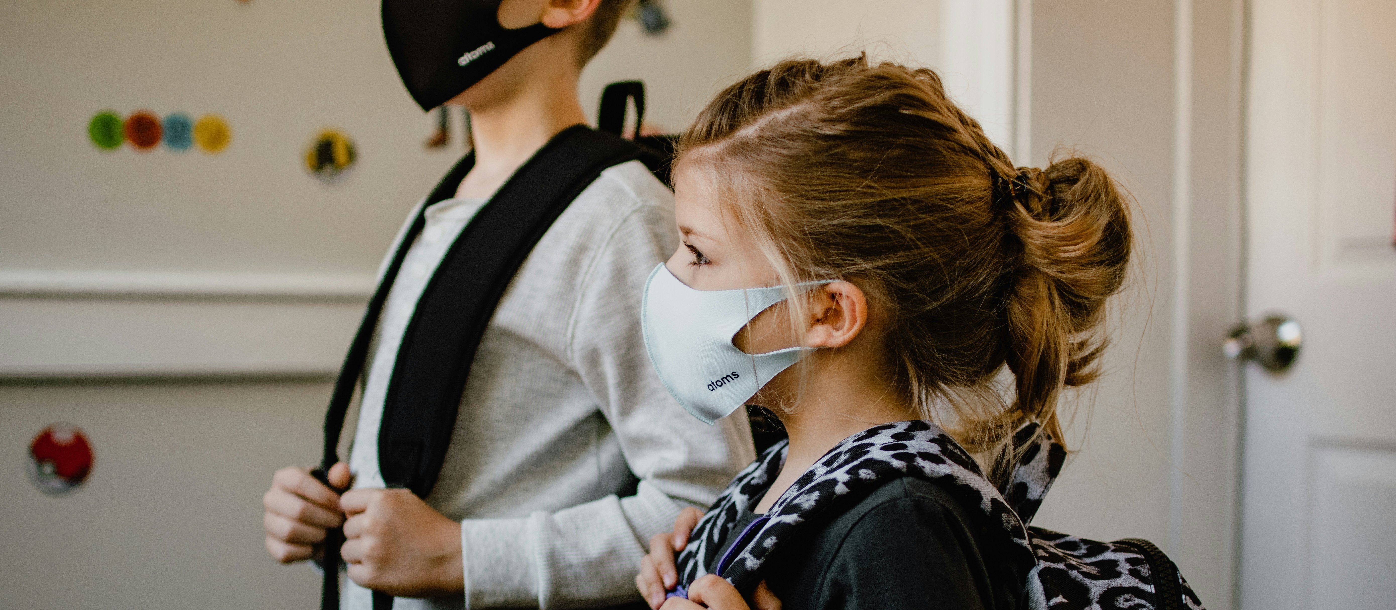 Two children wearing protective masks, with schoolbags on their backs