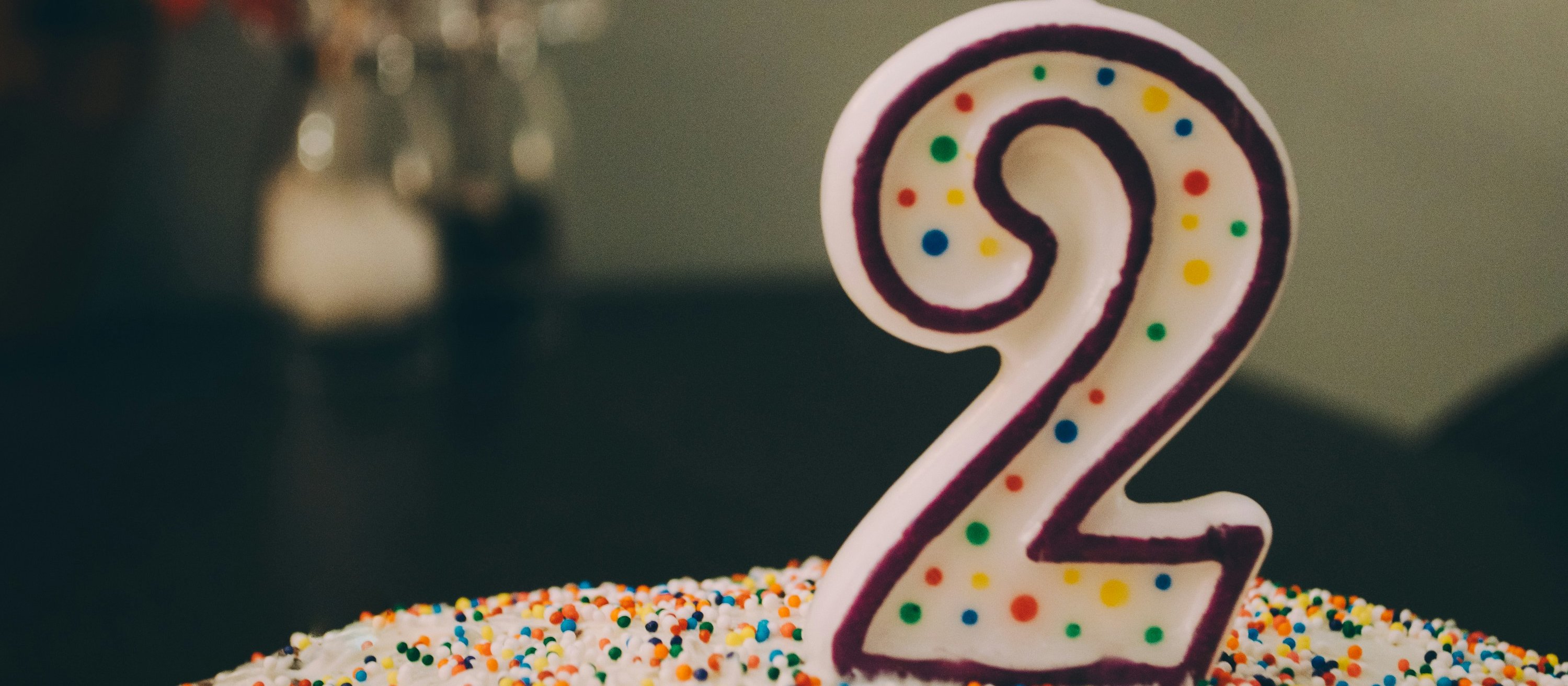 A birthday cake covered in rainbow-sprinkles with a number 2 candle on top