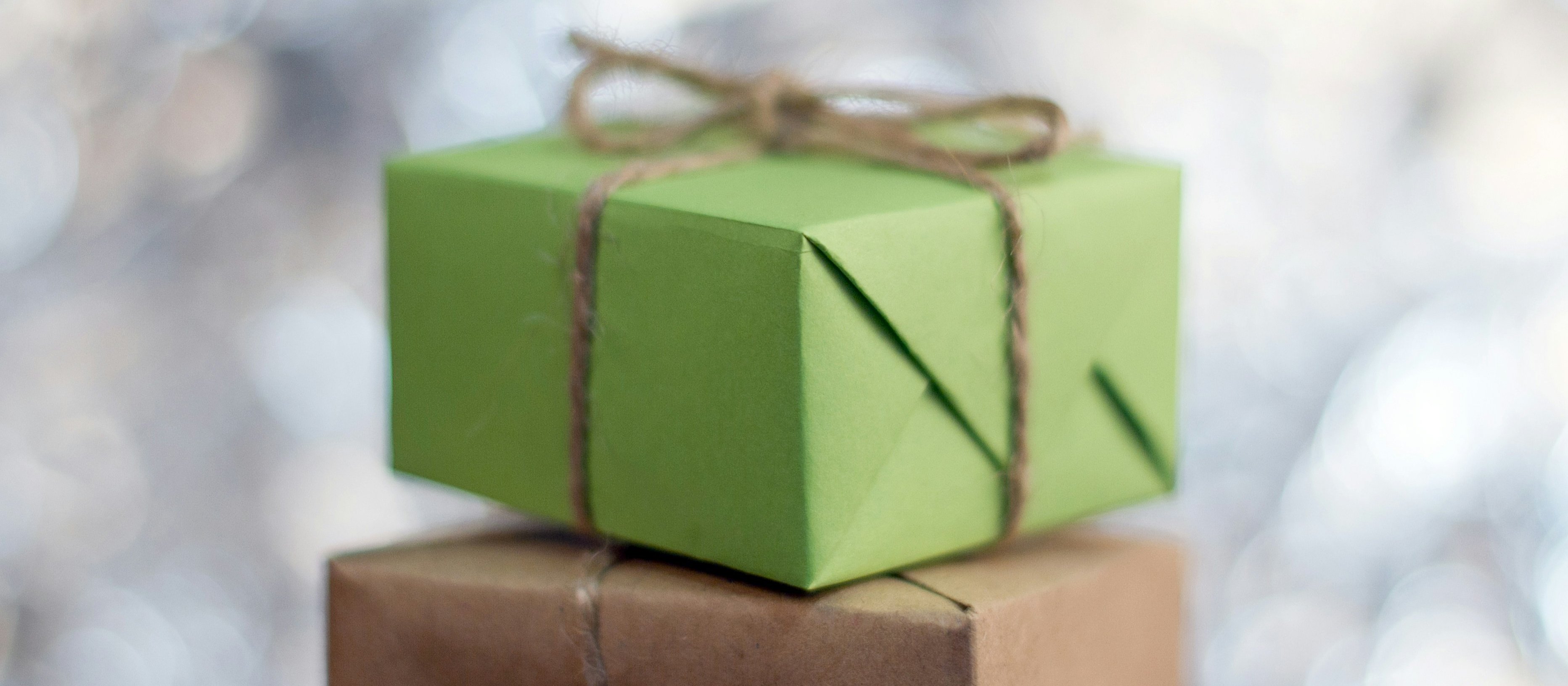 A brown paper parcel wrapped in string, with a green parcel sitting on top 