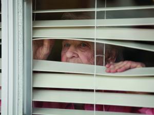 Elderly woman looks through blinds