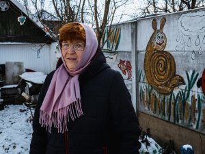 68-year-old grandmother, Larysa-, standing in the yard of her house in Ukraine in front of a wall that she painted [Image: Olena Dudchenko/Save the Children]