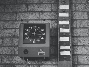 Image in black and white shows an employee time card machine beside a row of time cards