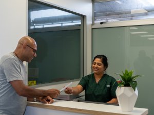 Image shows a man at the reception desk of Connect Radiology, with woman behind the counter reaching for his referral papers