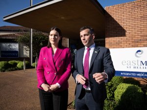 Image shows Brooke van Velden in bright pink blazer and black trousers standing beside David Seymour in a dark suit and pink tie, outside a redbrick medical centre