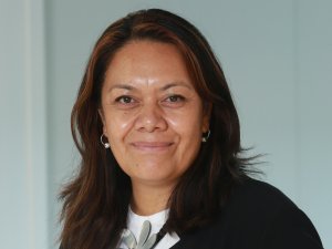 Margie Apa, wearing a white top with a flower and black blazer, smiling at camera