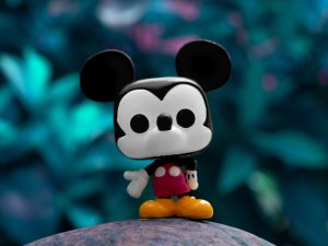 A small Mickey Mouse toy set on a rock, with foliage in background