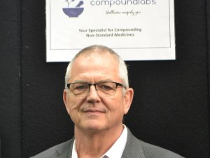 Man with glasses looking at camera, sign above head reads Compound Labs