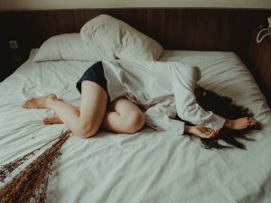 Woman lies on a bed, with her hands over her head