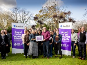 A group of people standing on lush grass, two in the middle holding up a framed certificate