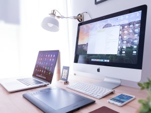 A desk with digital devices, including an Apple mac, a laptop, and a phone