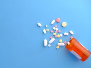 Different coloured pills spilling out of a medication jar on a blue background