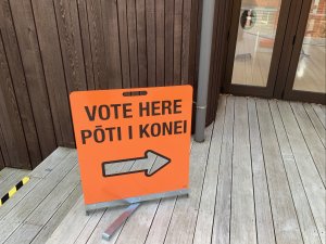 An orange sign reads 'vote here pōti i konei' with a clear cut arrow pointing to a door on the right