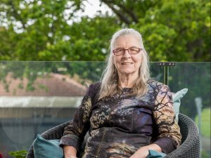 Amanda Oakley sits in a black rattan chair with trees in background