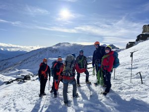 Photo shows group of people in mountaineering gear standing on a snowy mountain 