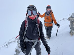 Two women in mountaineering gear hiking on a snowy mountain, with snow falling around them