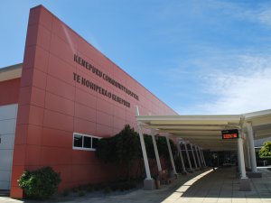 Side-view of Kenepuru Community Hospital, red-clad building with the name in large black writing on the front. White covered footpaths and a bus stop sign out the front