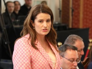 Woman with brown hair in pink check blazer, talking