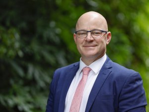 Matt Doocey, wearing blue blazer, white shirt and light pink tie, trees in background