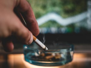 A hand holding a lit cigarette towards an ashtray