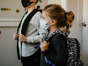 Two children wearing protective masks, with schoolbags on their backs