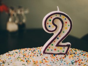 A birthday cake covered in rainbow-sprinkles with a number 2 candle on top