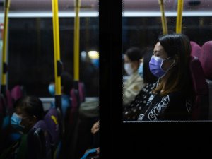 Woman with dark hair wears a mask on a bus