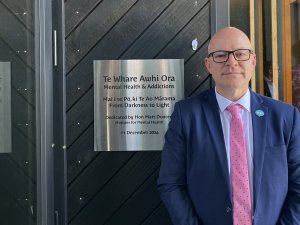 Matt Doocey, in navy suit and pink tie, standing beside a plaque marking the opening of a new mental health unit at Gisborne hospital